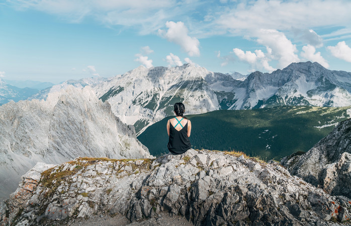 Eine Frau geniesst eine Pause auf dem Jakobsweg zwischen dem Bodensee und Genf und schaut sich bewundernd das Bergpanorama an