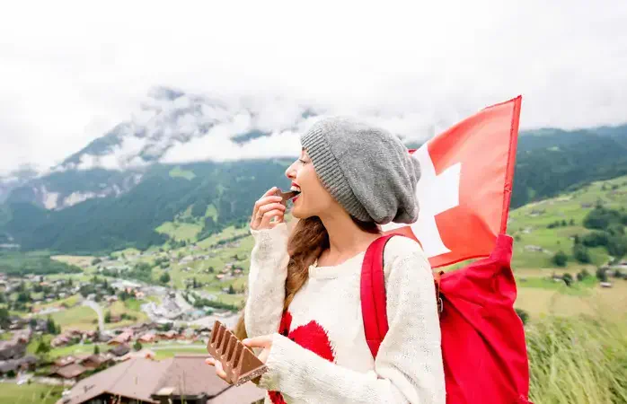 Young woman with swiss flag eating chocolate outdoors in the mountains. Having great vacations in Switzerland